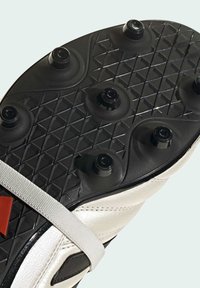 Suela de zapato de fútbol con goma negra, seis tacos y un patrón texturizado. Presenta una parte superior de cuero blanco y una correa gris en el medio.