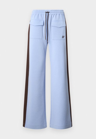 Light blue sweatpants with a drawstring waistband, broad brown side panels, and two front pockets. Features a logo on the left thigh.