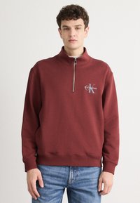 Μπορντό φούτερ με φερμουάρ, κατασκευασμένο από μείγμα βαμβακιού. Διαθέτει ριμπ μανσέτες, ψηλό γιακά και κεντητό λογότυπο στο στήθος. Χαλαρή εφαρμογή.