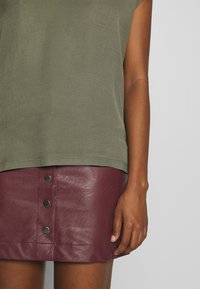 Oliven grøn ærmeløs top parret med en bordeaux læder miniskirt med tre sorte metalknapper ned foran.