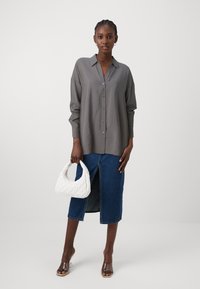 Camisa cinza de botões com mangas longas, combinada com uma saia de ganga com uma fenda à frente. Bolsa branca acolchoada e sandálias de salto transparente.