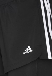 Gros plan sur un short de sport noir Adidas avec trois bandes blanches et le logo Adidas près de l'ourlet.