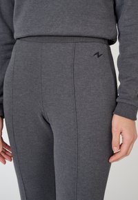 Leggings deportivos grises hechos de una tela suave y texturada. Presentan un diseño ajustado, costuras laterales y un pequeño logo acentuado en la parte de la cadera.