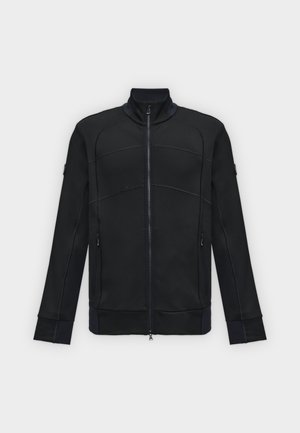 Chaqueta negra de manga larga con cuello alto, cremallera delantera, costuras curvas en los paneles y dos bolsillos con cremallera, sobre un fondo claro.