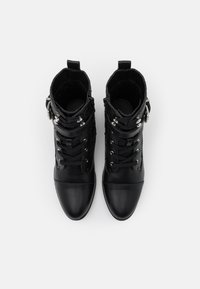 Bottines noires avec une finition en cuir lisse, dotées de laçages sur le devant, d'accents en métal et de détails texturés sur le dessus.