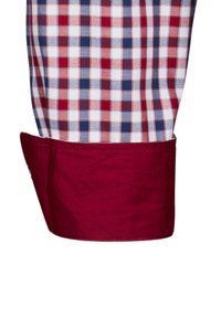 Camicia a quadri con motivi rosso, bianco e blu; presenta un polsino bordeaux; il tessuto sembra intrecciato e testurizzato.