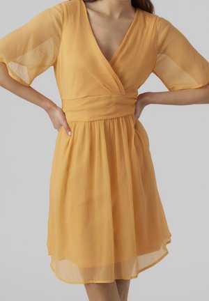 Kortærmet kjole med dyb V-udskæring i blødt gult stof med plisseret tekstur, markeret talje og flydende nederdel, der falder over knæene.