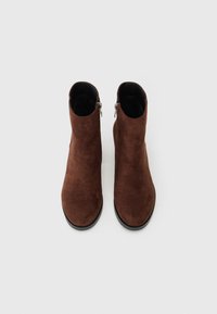 Braune Wildleder-Stiefeletten mit glatter Textur, runder Zehenform und seitlichem Reißverschluss. Erhöhung auf einer flachen schwarzen Sohle.