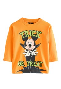 Orange bomulds t-shirt med rund hals, med en tegneseriefigur og teksten "TRICK OR TREAT" i fed grøn skrift.