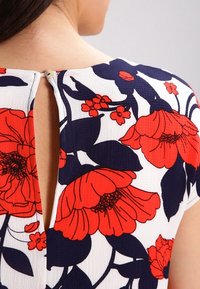 Vestido floral con fondo blanco y grandes flores rojas y marinas. Espalda con abertura en forma de llavero y cierre de botón. Tejido suave y texturizado.