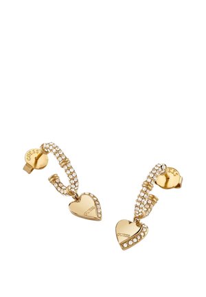 Kolczyki na sztyft marki Guess w złotym odcieniu, z zakrzywionym wzorem zdobionym kryształkami oraz wiszącymi złotymi serduszkami z wygrawerowanym napisem "GUESS".