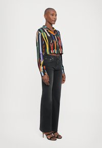 Camicetta multicolore tagliata con strisce verticali, jeans larghi in denim nero e tacchi a strappi neri. Tessuto morbido e vestibilità su misura.
