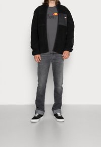 Černá fleecová bunda na zip, šedé tričko s logem, tmavě šedé džíny a černé tenisky s bílou podrážkou. Jednoduchý, ležérní design.