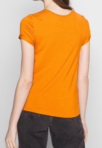 Oranžové tričko s krátkým rukávem vyrobené z jemné bavlny, s kulatým výstřihem a slim fit, nošené s tmavě šedými džíny.