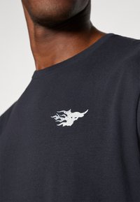 Navy blue t-shirt in cotton blend, featuring a white graphic design of flames on the left chest area. Classic crew neck and short sleeves.