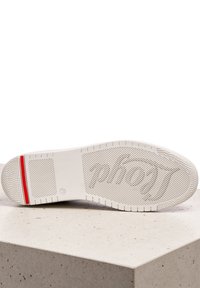 Bílá guma podešve tenisky s texturovaným gripem, s červeným akcentním proužkem a vyraženým logem. Plochý, hladký povrch pro stabilitu.