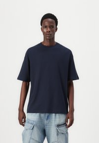 Tricou oversized de culoare bleu marin, cu mâneci scurte, guler rotund, fabricat din bumbac, având o textură fină și o croială lejeră.