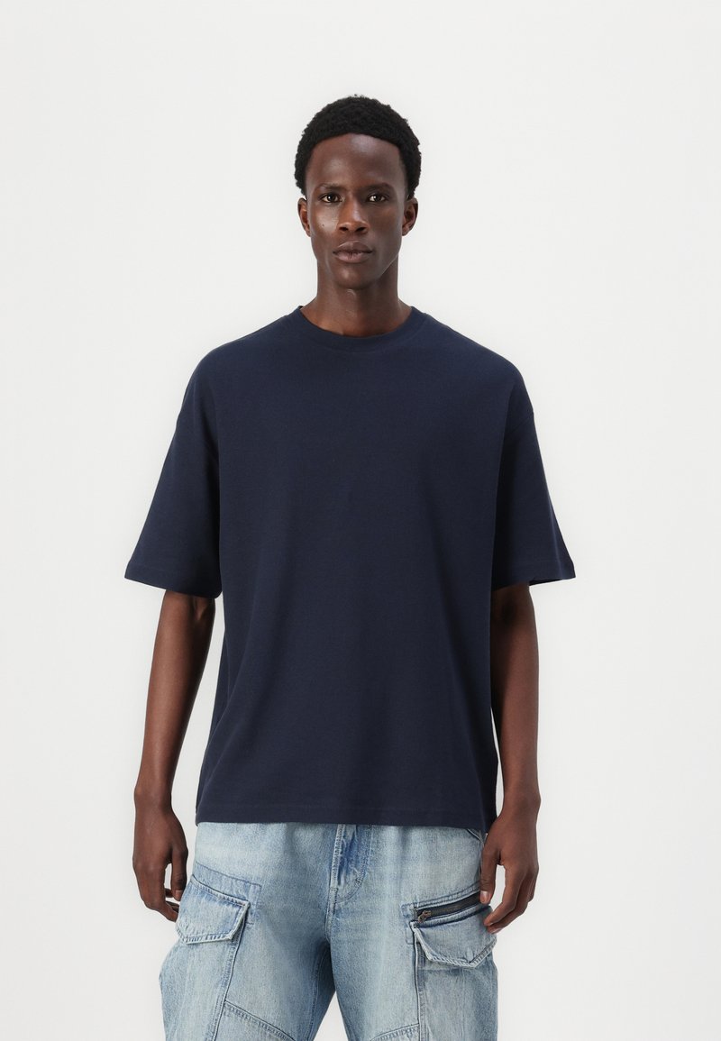 Tricou oversized de culoare bleu marin, cu mâneci scurte, guler rotund, fabricat din bumbac, având o textură fină și o croială lejeră.