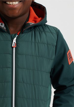 Zielona kurtka puchowa o pikowanej strukturze, z jasnopomarańczowym kapturem podszewkowym i białym zamkiem błyskawicznym. Pomarańczowy akcent z logo na rękawie.