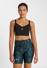 Schwarzer Sport-BH mit V-Ausschnitt und verstellbaren Trägern, kombiniert mit eng anliegenden Shorts mit dunkelgrünem und schwarzem Wellenmuster.