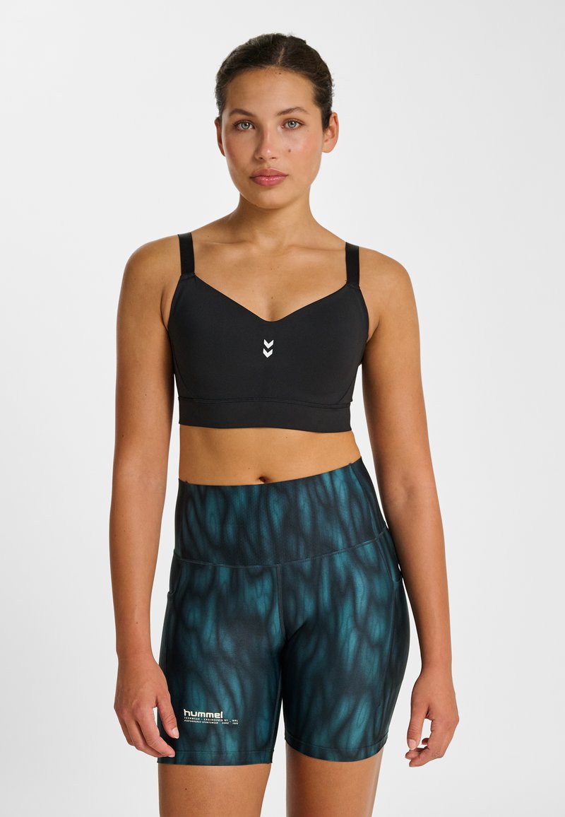 Schwarzer Sport-BH mit V-Ausschnitt und verstellbaren Trägern, kombiniert mit eng anliegenden Shorts mit dunkelgrünem und schwarzem Wellenmuster.