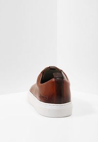 Braune Leder-Sneaker mit glatter Oberfläche, weißer Gummisohle und dunkler brauner Ferse; minimalistisches Design mit subtiler Markenkennzeichnung.