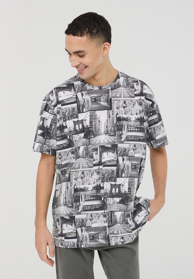 T-shirt grafico con un collage fotografico in bianco e nero, maniche corte, collo rotondo e vestibilità ampia. Il materiale sembra morbido e leggero.