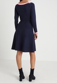 Navy blue dress with a flared skirt, long sleeves, and a rounded neckline featuring red and white stripes at the collar and cuffs.