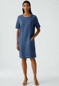 Kurzes ärmelloses Kleid aus blauer Stoff, mit rundem Ausschnitt, seitlichen Taschen und lockerer Passform, das gerade über dem Knie endet.