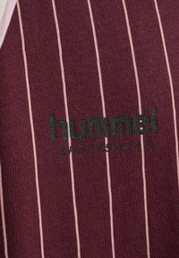 Bordeaux sportsskjorte med vertikale lys rosa striber, med tekstureret stof og et trykt logo "hummel SPORTSWEAR" i mørkegrøn.