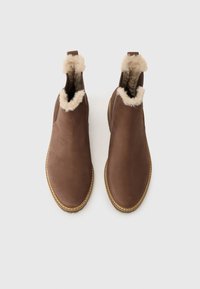 Botas de cuero marrón hasta el tobillo con un forro beige suave en el cuello, textura lisa, punta redondeada y detalles de costura a lo largo de la suela.