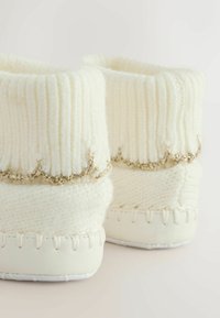 Kreemikootud sussid ribatekstuuriga, kaunistatud õrna kuldse äärega, pehme valge nahkse tallaga ja õmblusaktsentidega.