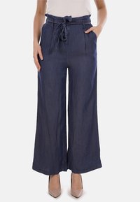 Pantaloni a gamba larga in denim scuro, dotati di vita a sacchetto con cintura da annodare, due tasche laterali e una texture liscia.