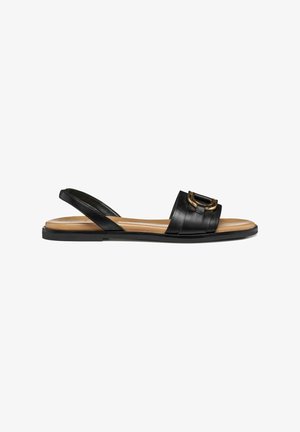 Sandali slingback in pelle nera con una larga fascia decorata con fibbia color oro, suola piatta e design minimalista.