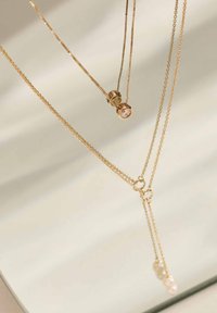 Gouden kettingen met delicate schakels en ronde hangers. Eén ketting heeft aan het einde drie kleine decoratieve kralen. Glad, glanzend oppervlak.