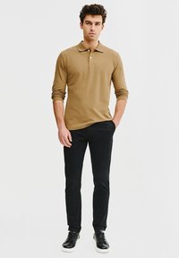 Beżowa koszula polo z długim rękawem i kołnierzykiem, w połączeniu z czarnymi spodniami w slim fit oraz czarnymi sneakersami. Prosty design, miękka tekstura i dopasowany krój.