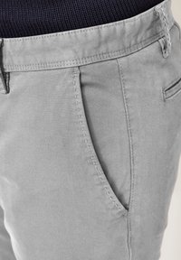 Gray cotton chinos with a smooth texture, featuring a side pocket and subtle stitching. Waistband is elastic knit.