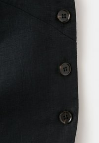 Tissu noir avec trois boutons noirs brillants alignés verticalement le long d'une couture sur un fond clair.