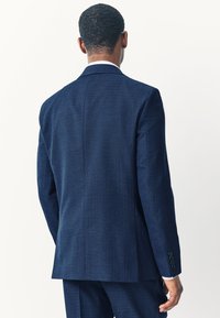 Veste de costume ajustée bleu marine avec un tissu texturé, fente simple et poignets à quatre boutons, vue de dos.