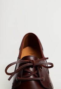 Chaussure en cuir marron à bout rond, design à lacets, détails cousus et texture lisse. L'int érieur est beige avec des accents minimalistes.