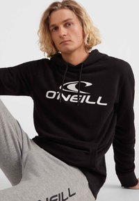 Čierna mikina s kapucňou a logom O'Neill, s tiahnućou kapucňou, príjemný na dotyk; v kombinácii s sivými teplákmi s detailom loga.