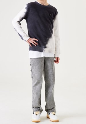 Felpa tie-dye grigia scura e bianca con polsini a costine, indossata sopra una maglietta bianca a strati, abbinata a pantaloni dritti grigi chiari e sneakers.