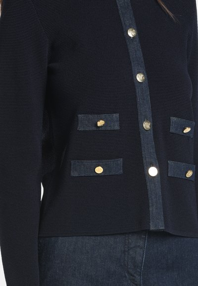 Tengerészkék kötött kardigán farmer részletekkel, arany gombokkal és két rávarrt zsebbel. Texturált anyag, strukturált szabással.