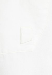 Witte stof met een gestructureerd oppervlak. Bevat een klein, vierkant, geborduurd label in een iets contrasterende witte draad aan de linkerkant.