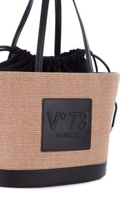 Bolso de tote de paja trenzada con base de cuero negro, que presenta un interior de tela negra fruncida y un parche de logo grabado en la parte frontal.