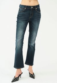 Tmavomodré rifľové nohavice so slim fit strihom, skrátenými zakrivenými nohavicami, dizajnom s piatimi vreckami a kontrastným šitím. V kombinácii s čiernymi topánkami na podpätku.