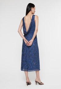 Modré flitrované šaty s hlubokým V-vzadu, mají přiléhavý design a jemné diamantové vzory. Délka ke kolenům s hladkým povrchem.