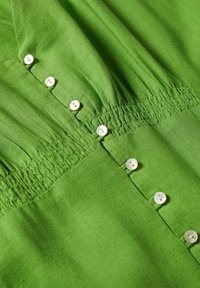Tissu vert en gros plan avec petits boutons blancs et détail de couture élastique froncée.