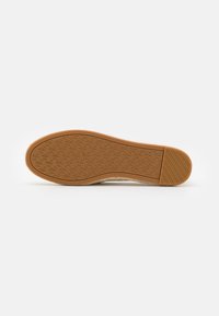 Suela de goma con un patrón texturizado, material superior de un beige claro y diseño plano. Cuenta con una puntera y un talón reforzados para mayor durabilidad.