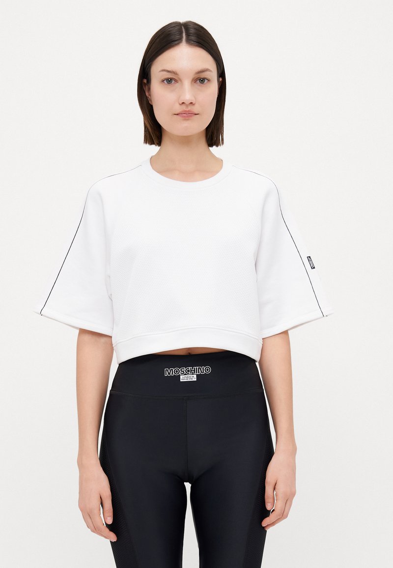 Vit kortärmad sweatshirt med strukturerad tyg, korta ärmar och svarta detaljer i sömmen. Kombinerad med högmidjade svarta leggings med en logotyp.